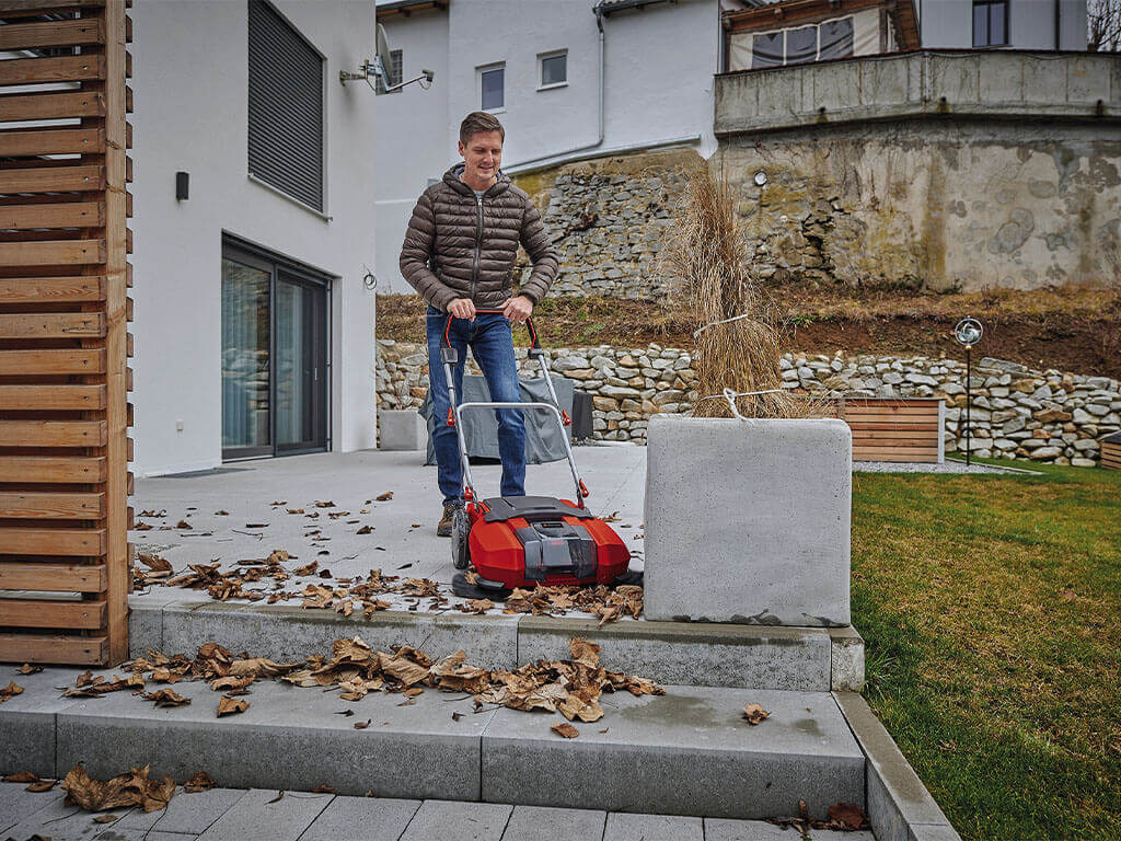 A man cleans his terrace with the help of the Einhell cordless push sweeper.