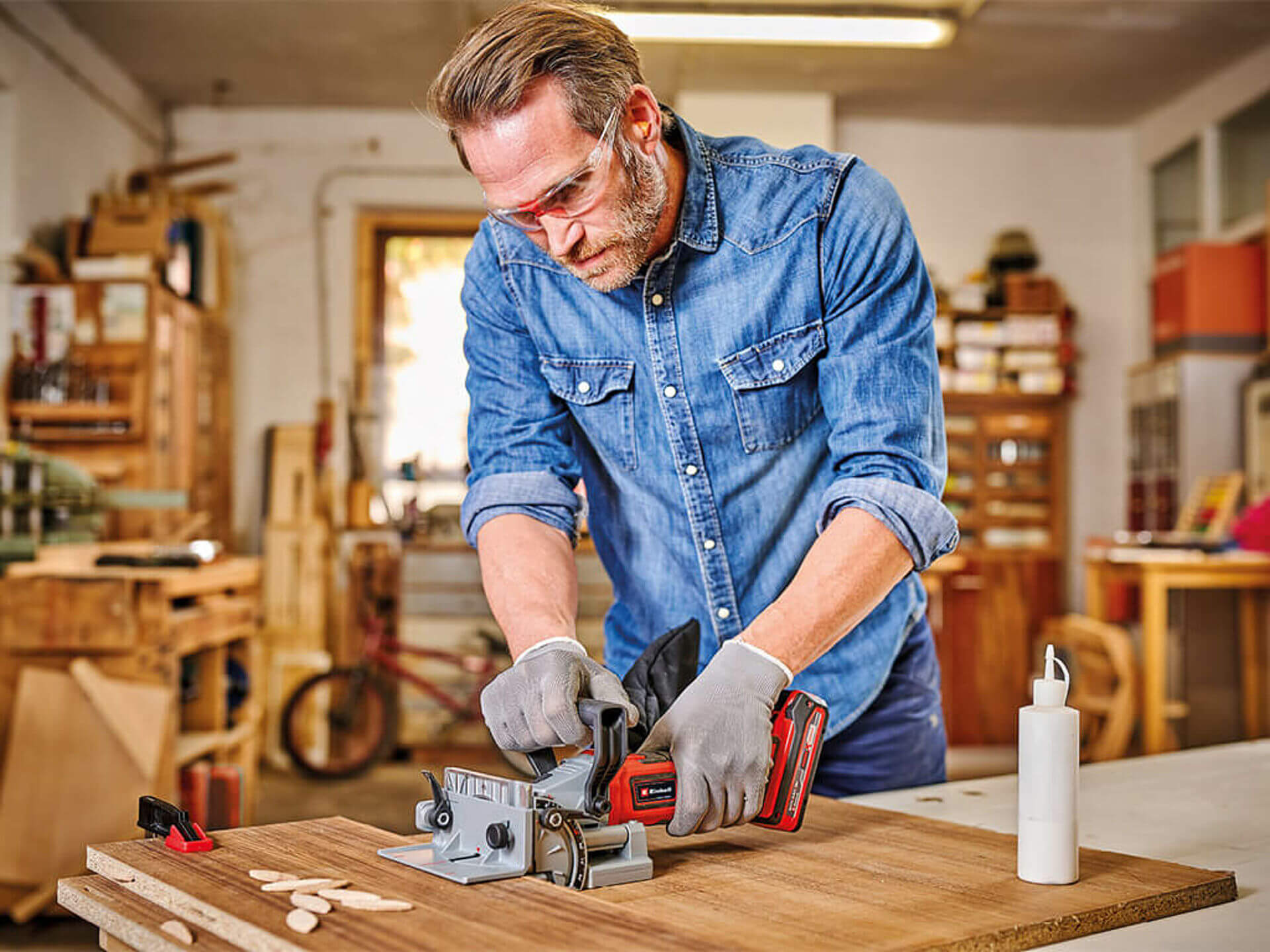 A man cuts a groove in a wooden board using the cordless flat dowel router from Einhell.