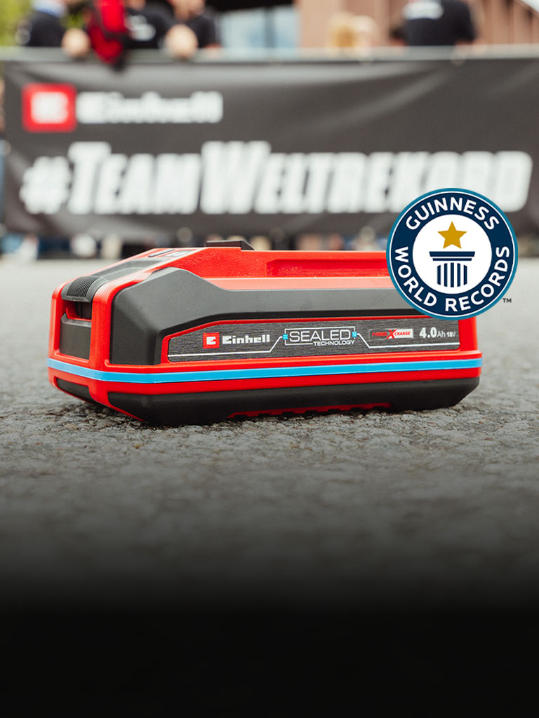 Batería Einhell SEALED Power X-Change 4.0 Ah sobre asfalto, con el logo de Guinness World Records "Record Holder" a la derecha.